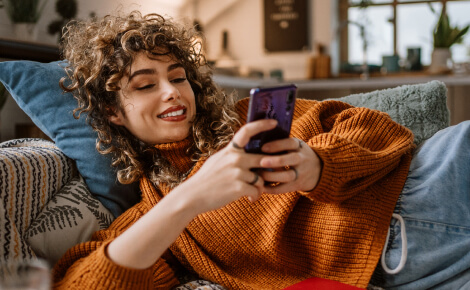 Young woman laying on a couch and using a smartphone