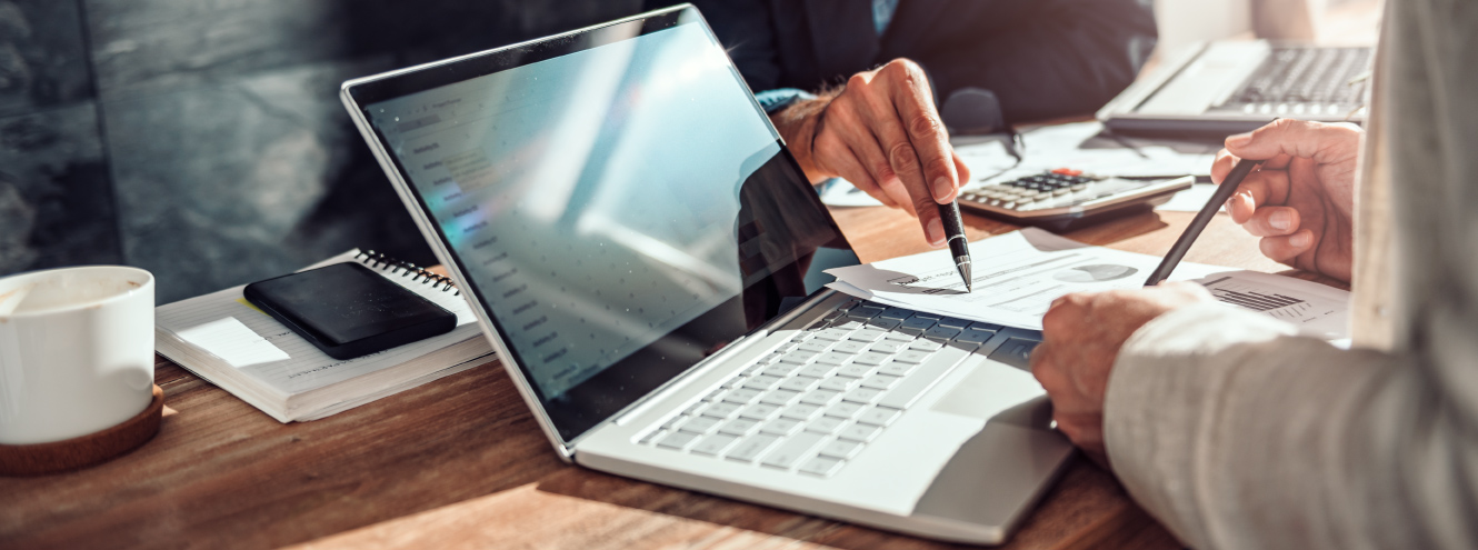 Two people looking a documents in front of a laptop